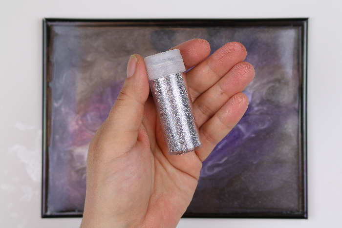 hand holding silver glitter with a resin frame in the background
