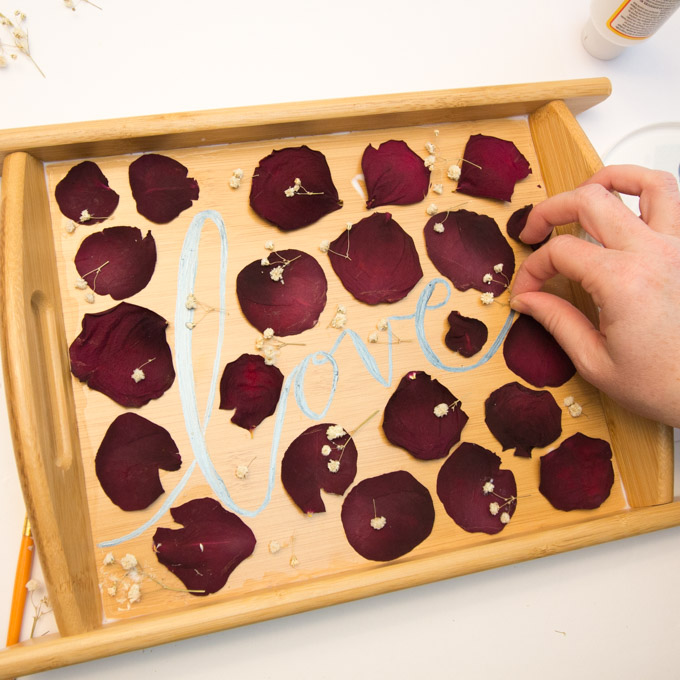 Arranging and pasting pressed rose petals and dried baby's breath onto a wooden serving tray