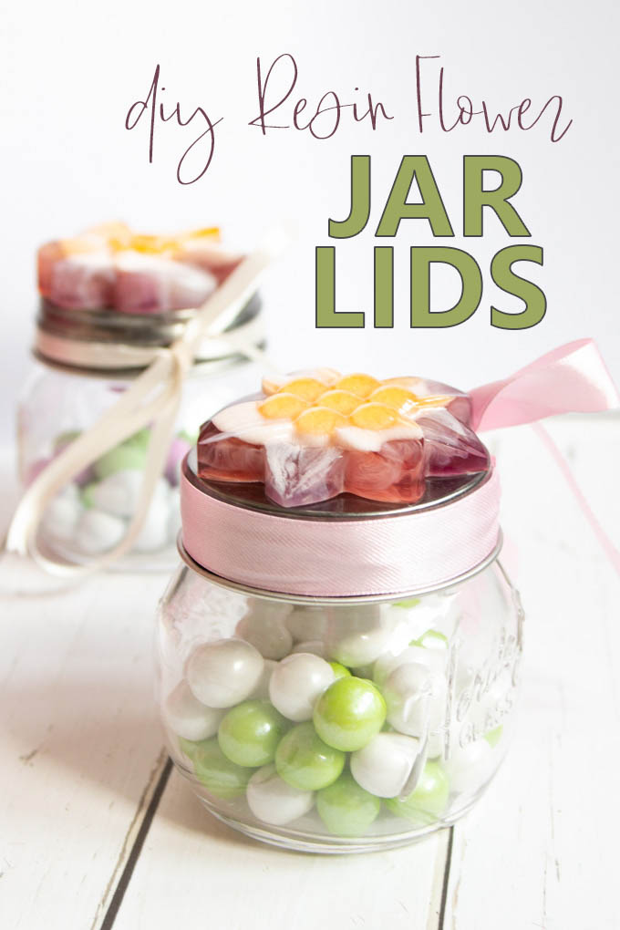 Small glass jars, topped with a handmade resin flower and filled with candies on a white wood surface.