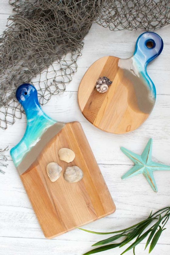 Two wood cutting boards with handles embellished with resin in a beach theme.
