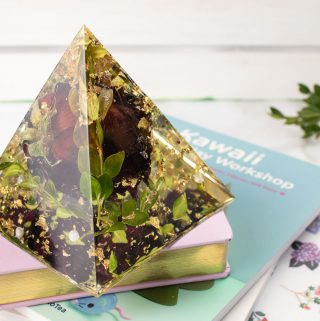 Resin pyramid with embedded rose, gold foil and boxwood leaves on a stack of books.