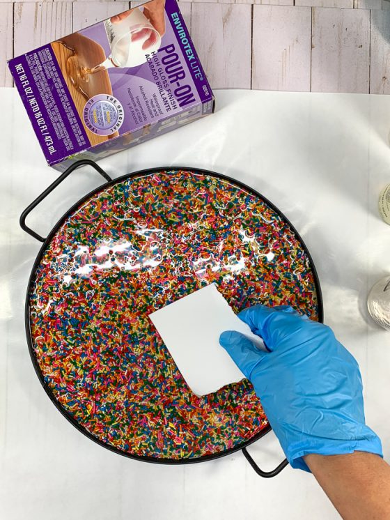 Use cardstock to spread EnviroTex Lite pour over resin onto the rainbow sprinkles.