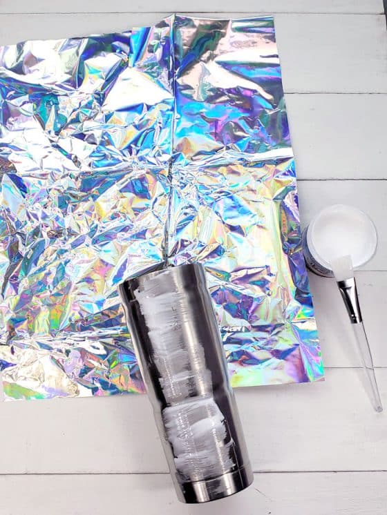 Begin by cutting a piece of the iridescent wrapping to fit around the tumbler. I found this iridescent table cloth at my local dollar store, it's a plastic tissue paper. I crinkled it up to give it texture and more refractive iridescent surfaces.