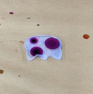 Purple alcohol ink dots in clear resin in a cat-shaped mold.